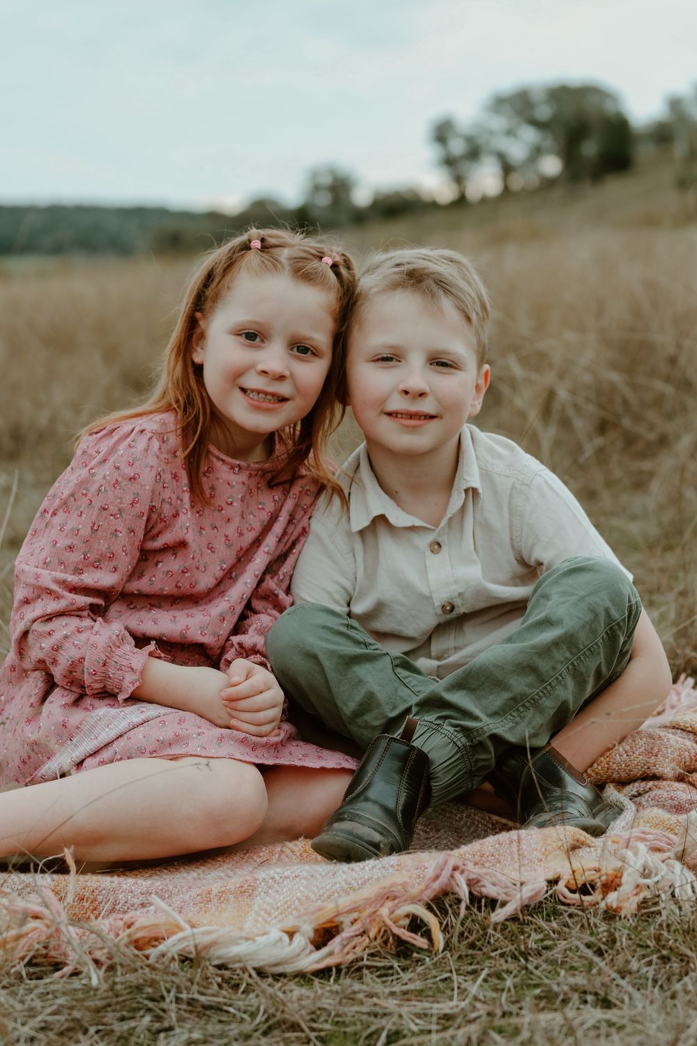 Two children laying in a sunlit field wearing vintage-style clothing in soft muted tones.