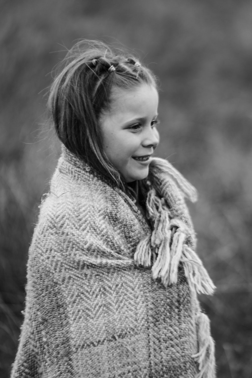 Young girl wrapped in a chunky knit shawl shown in a series of black and white portraits.
