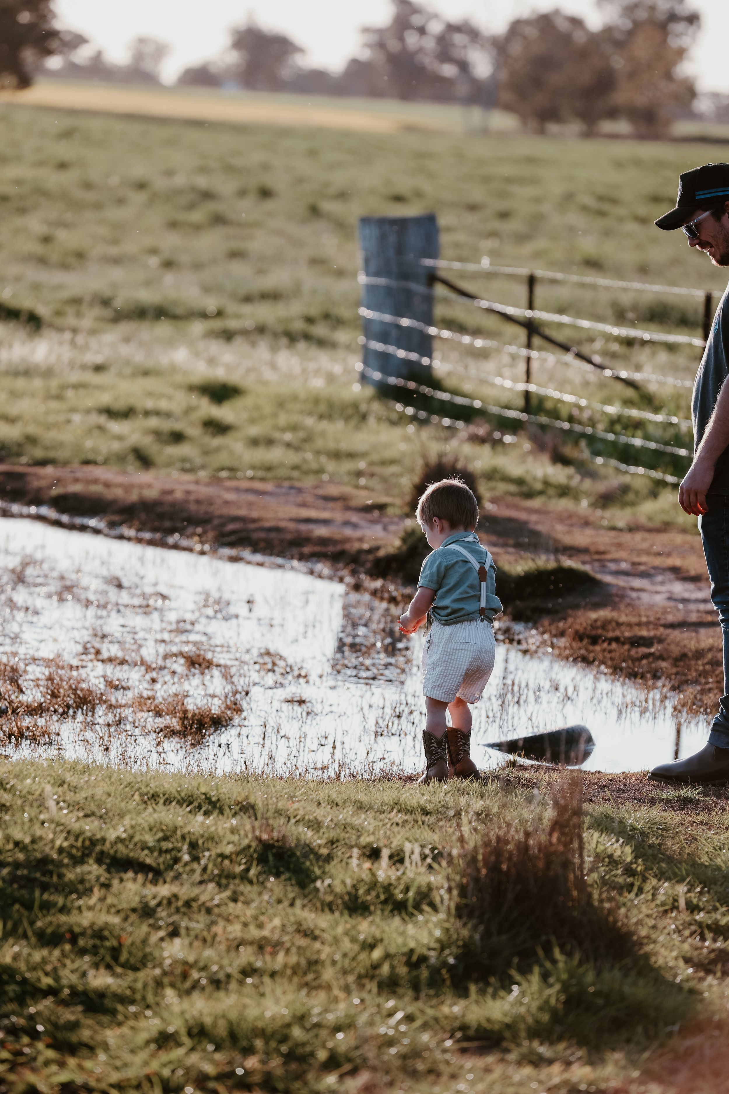 People exploring a shallow pond in grassy meadow landscape.