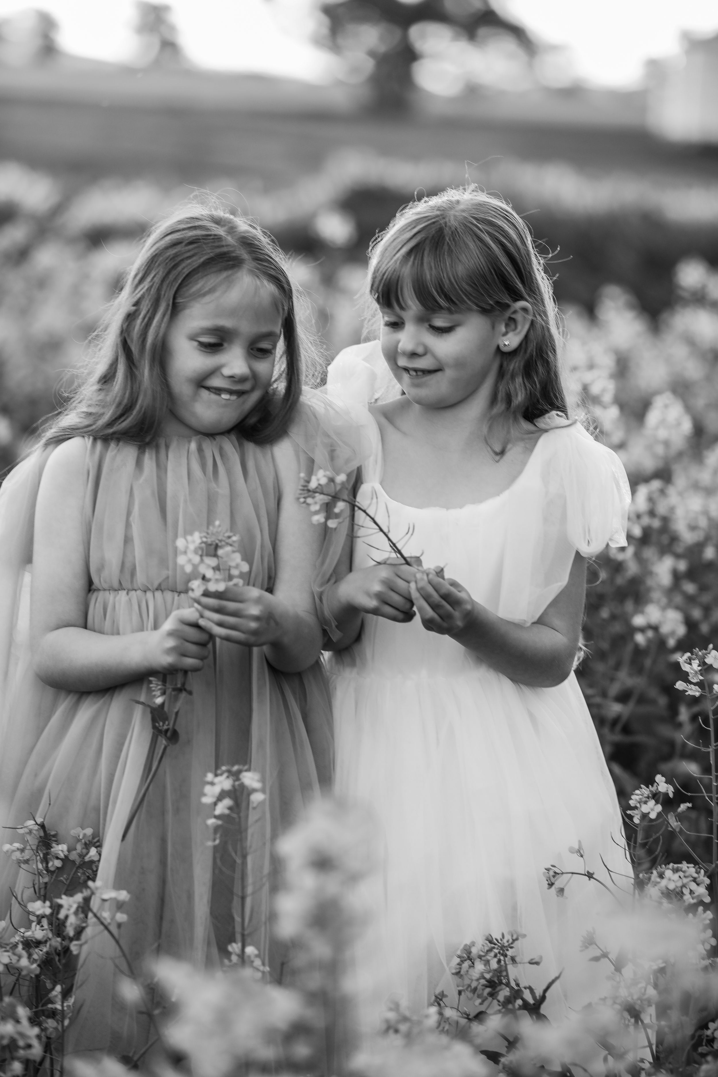 Black and white image of two young girls picking flowers in flowing dresses.
