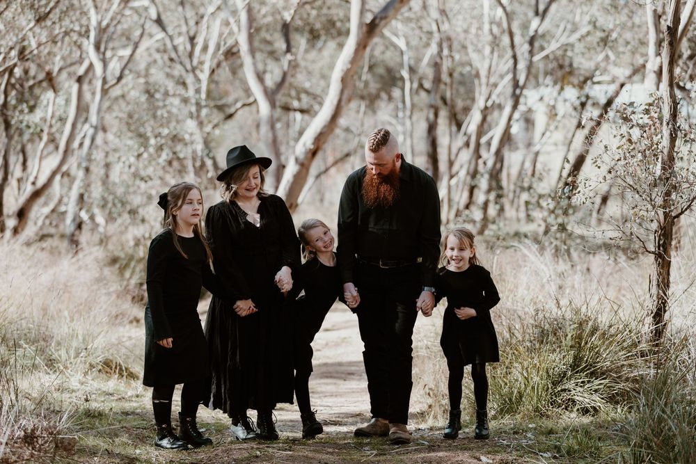 People dressed in black walking together through a wooded area in muted tones.