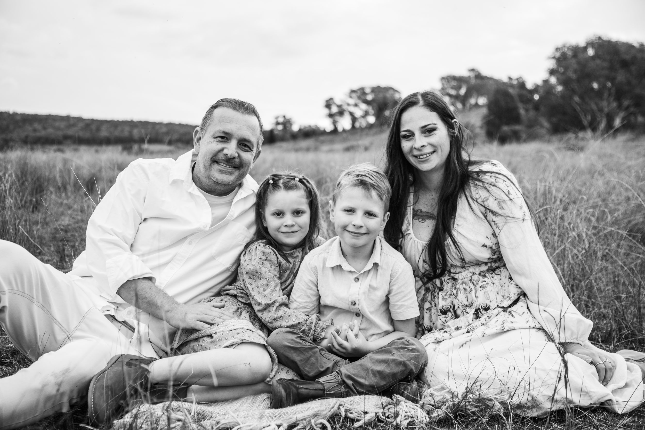 Family relaxing together on a blanket in an open field during golden hour.