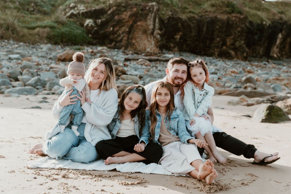 Family group lounging casually together on a sandy beach in coordinated casual outfits.