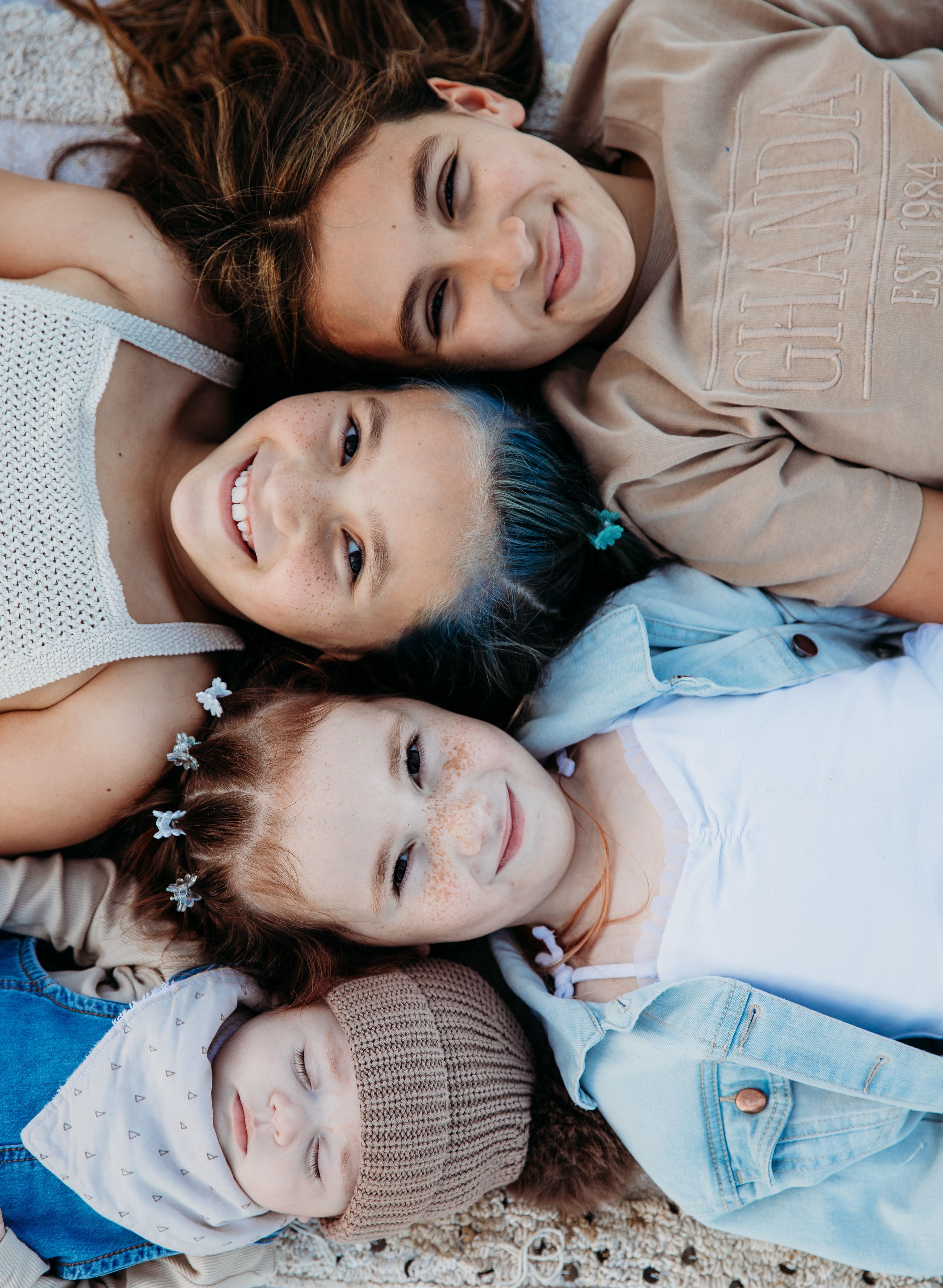 Family members lying together on textured ground in casual outfits of light blue and beige.