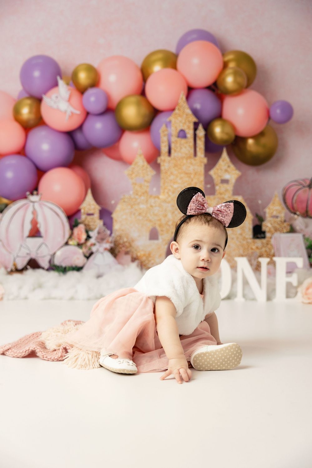 Pink and purple balloon arch with glitter castle backdrop creates magical first birthday party setup with princess theme decor.