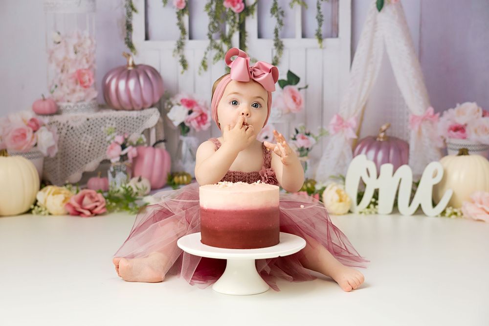 Pink and white cake smash photo setup with floral decorations, balloons, and vintage furniture for a first birthday celebration.
