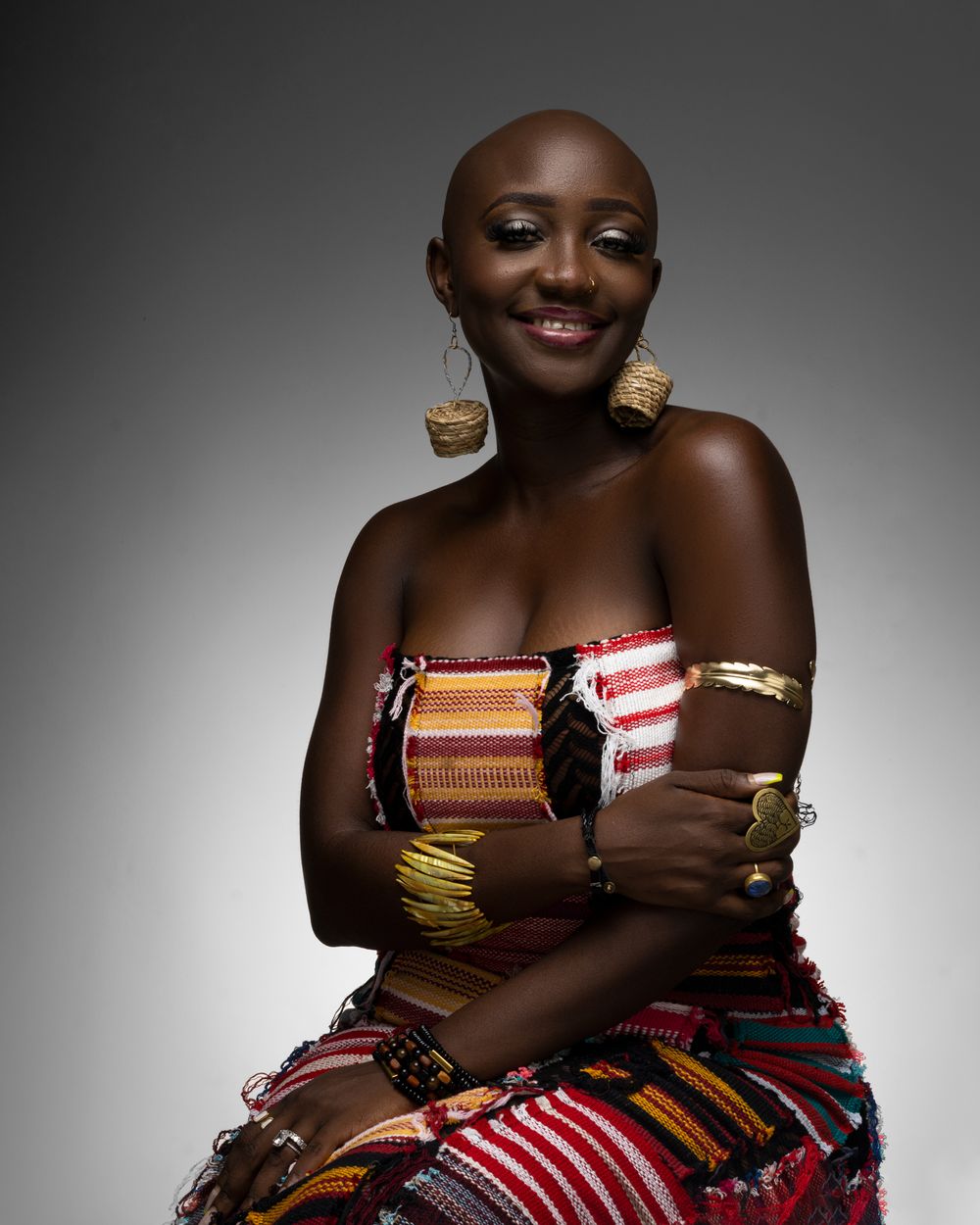A person wearing brightly colored traditional African-inspired clothing with striped patterns poses against grey backdrop.