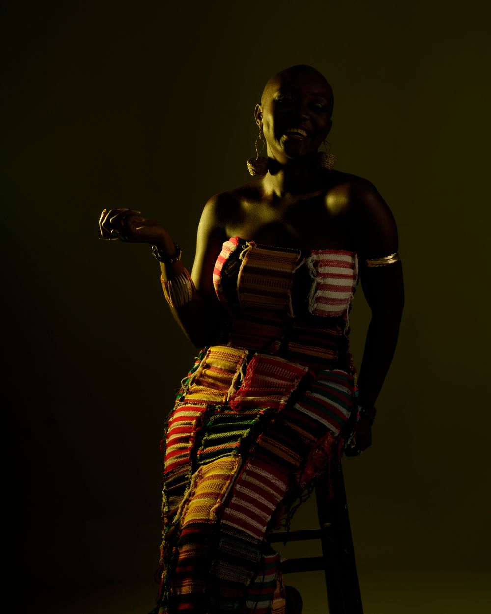 Dramatic low-key portrait showing silhouette in traditional African dress illuminated by warm directional lighting.