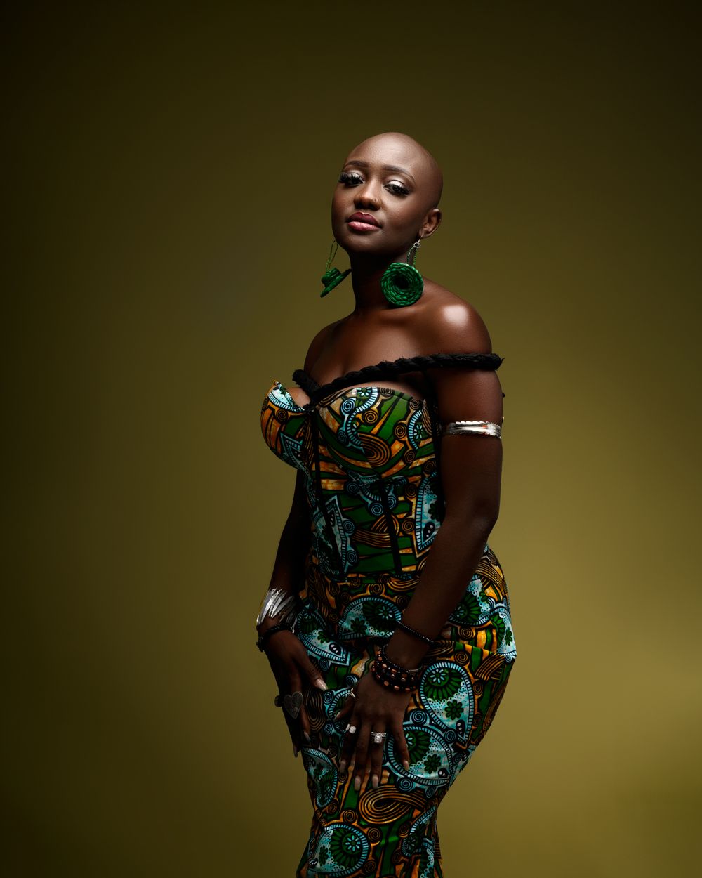 Elegant portrait against olive background showing model in green patterned off-shoulder dress and matching choker.