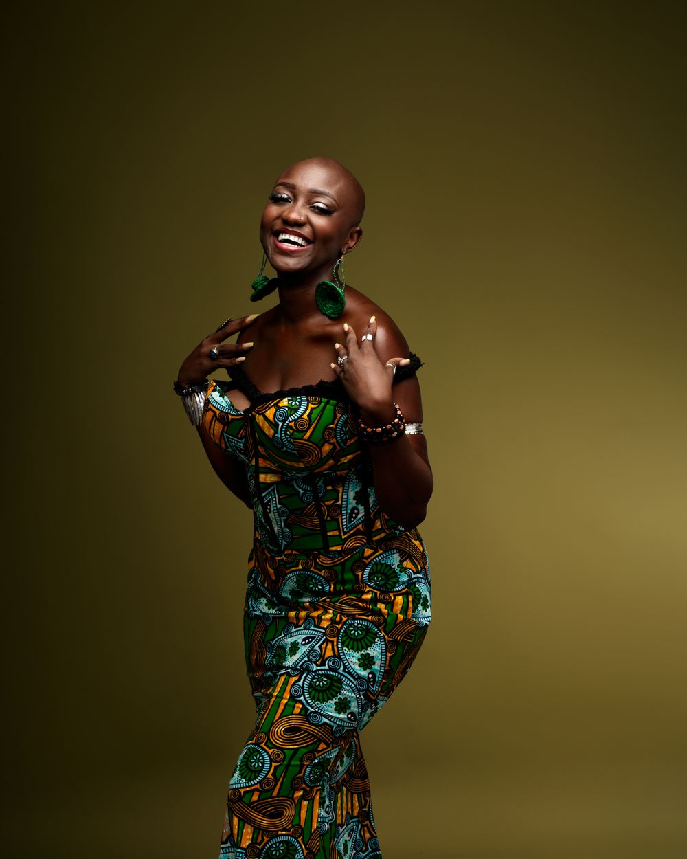 A joyful person wearing a vibrant patterned dress poses elegantly against a dark olive backdrop.