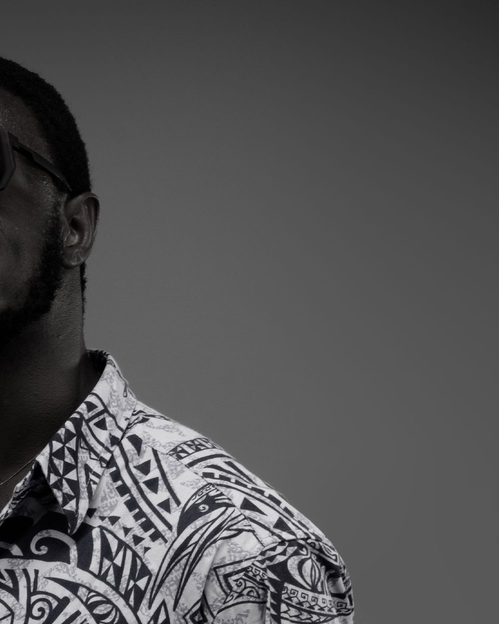 Monochrome photograph showing a person wearing a patterned shirt with tribal designs against a dark background.