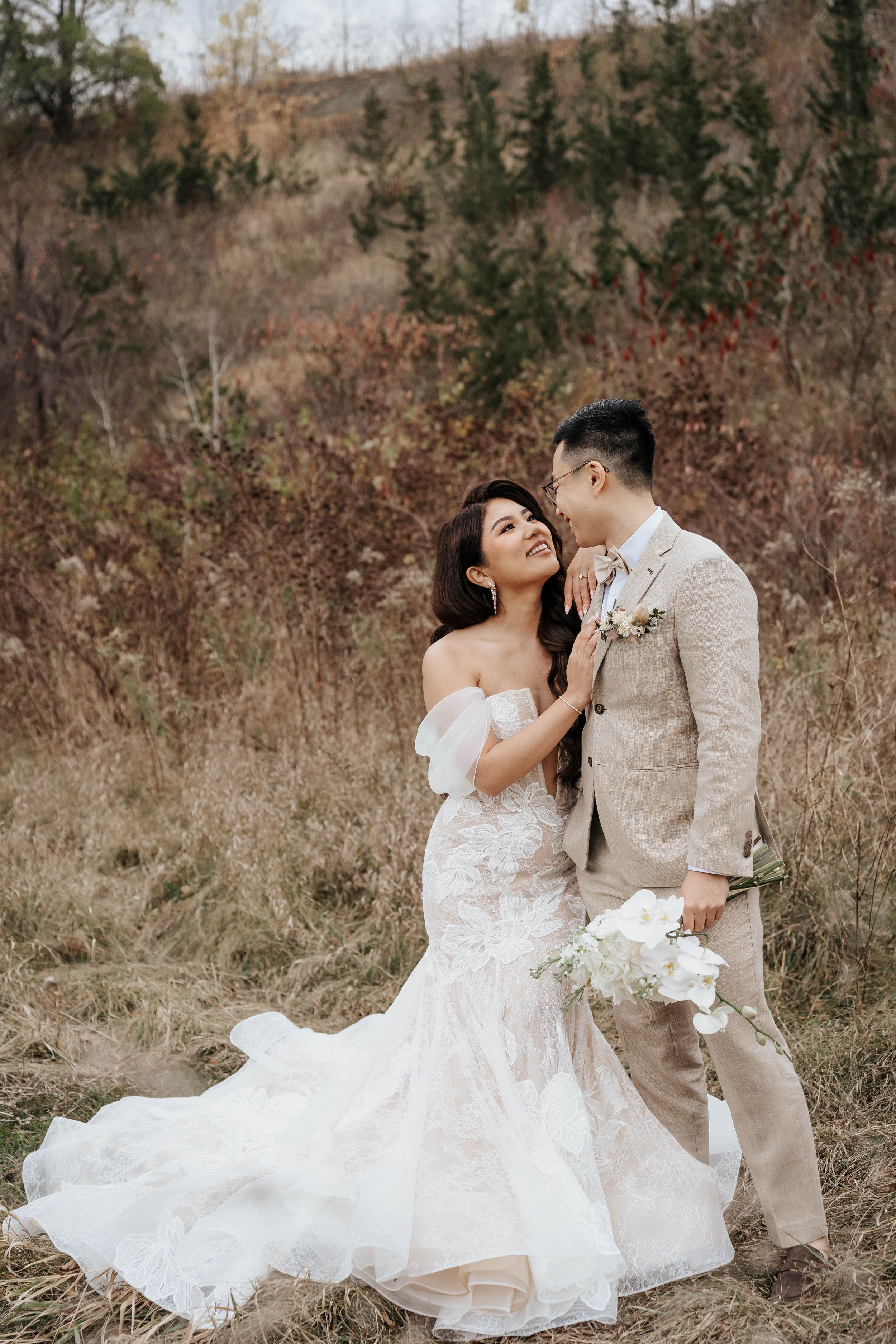 Romantic moment between newlyweds in autumn field with bride wearing lace gown.