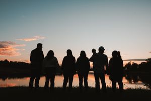 A series of silhouetted figures stand against a colorful sunset sky creating a dramatic panoramic view.