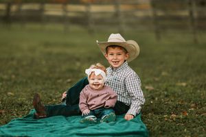 Family photo session in a grassy field with a blanket and casual country attire.