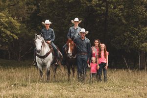 A group stands outdoors in western attire surrounded by trees and grassy fields during a photoshoot.