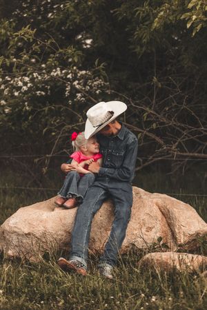 Two people sharing a tender moment while sitting on large rocks in nature, wearing denim and casual clothing.