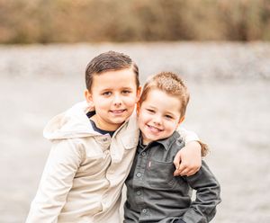 Two children sit together on a rocky beach wearing casual clothing and sharing a sweet moment outdoors.