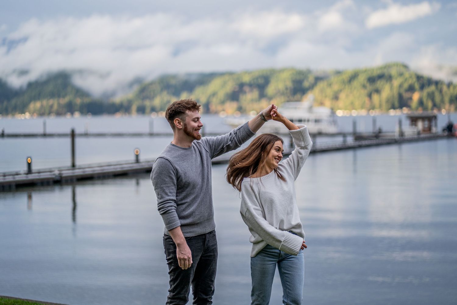A couple dancing together on a wooden dock by a peaceful lake with mountains in the background.