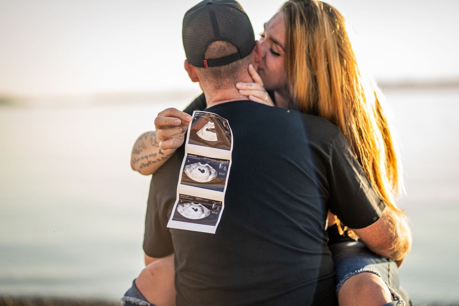 A couple holds an ultrasound photo while embracing in a tender moment during a pregnancy announcement photoshoot.