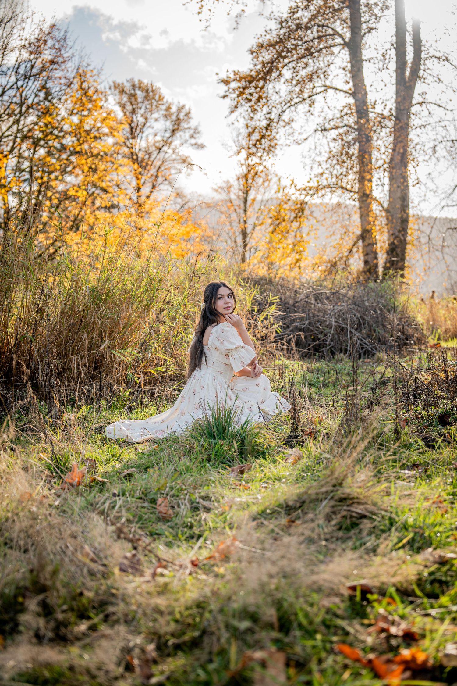 Ethereal autumn scene with person in white dress reclining among fallen leaves and tall grass at golden hour.