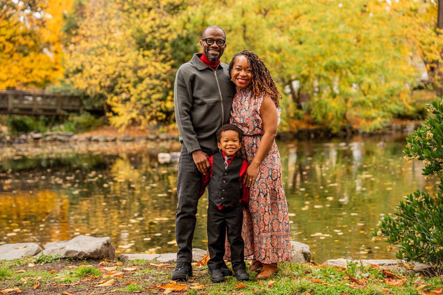 A couple shares a romantic moment surrounded by vibrant autumn foliage near a tranquil pond in a park setting.