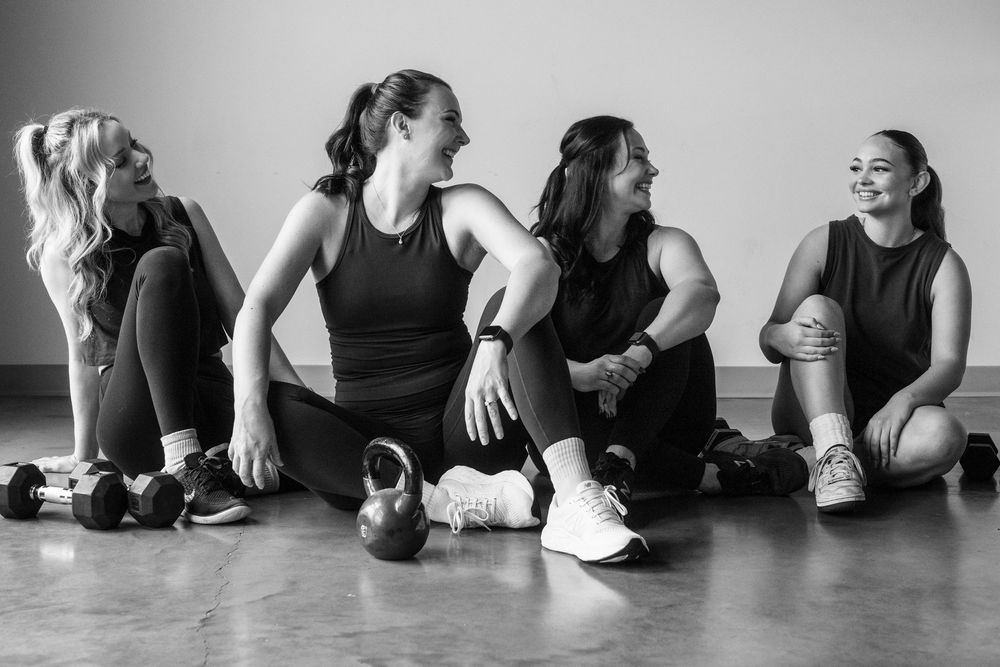 A black and white panoramic series of dancers sitting and stretching on the floor during rehearsal.