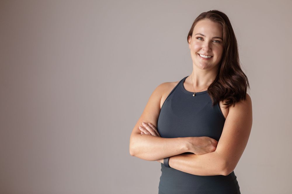 Woman in athletic wear smiles while sitting and posing against neutral background in studio setting.