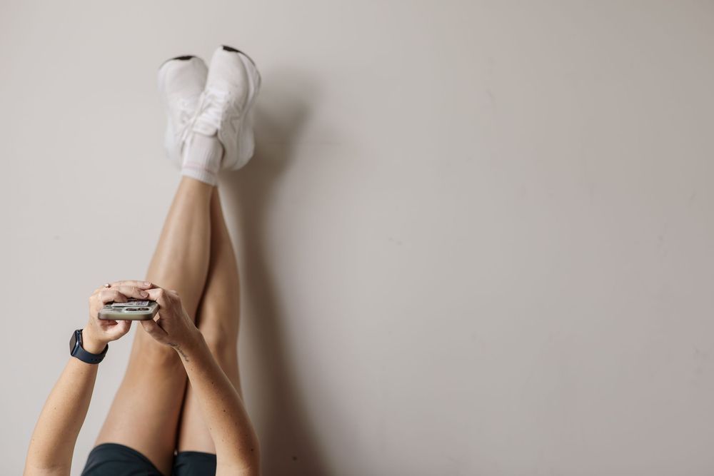 A person wearing white socks sits on a beige floor with their legs crossed in a minimalist setting.