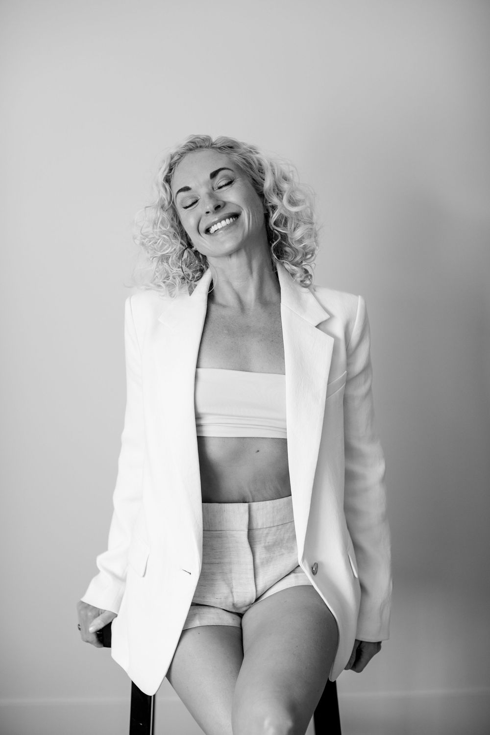 Four black and white artistic fashion photos featuring a white blazer and minimalist styling against a light background.