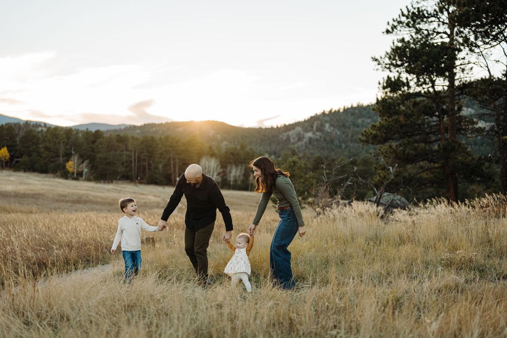 Family walking hand in hand through tall grass field at sunset with mountains in background.