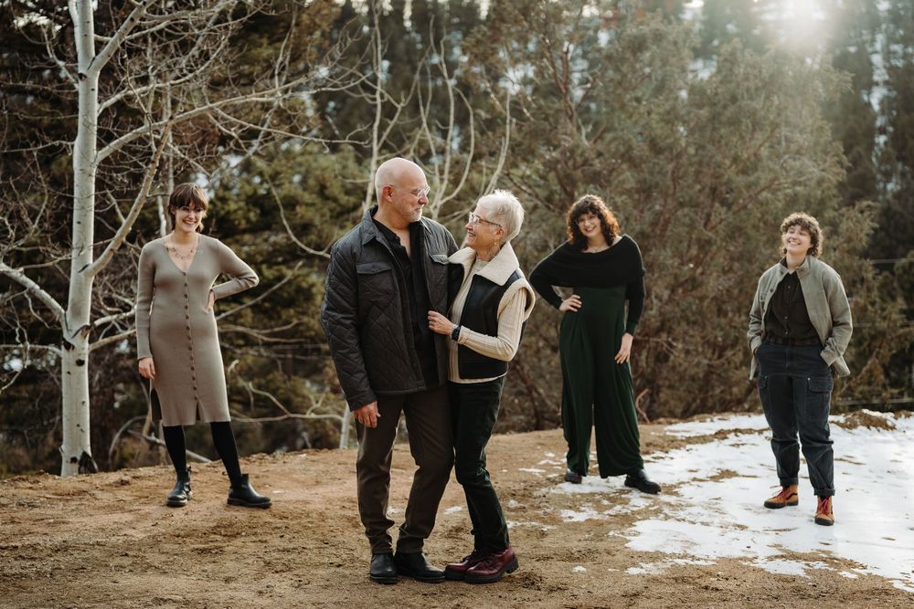 Family of five poses outdoors in winter woodland setting with snow-dusted ground and evergreen trees.