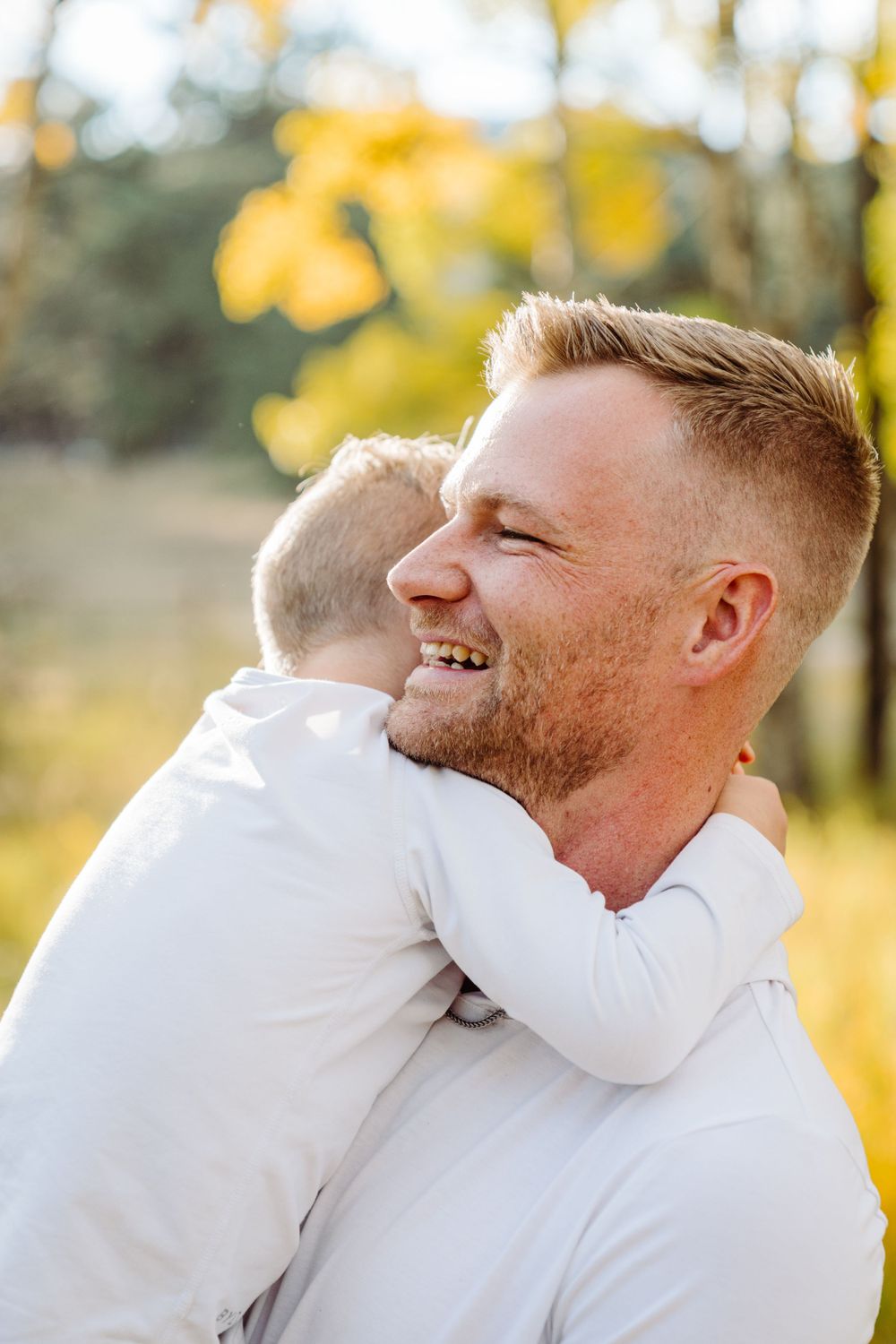 Father and child sharing a joyful embrace in autumn sunlight with golden leaves in background.