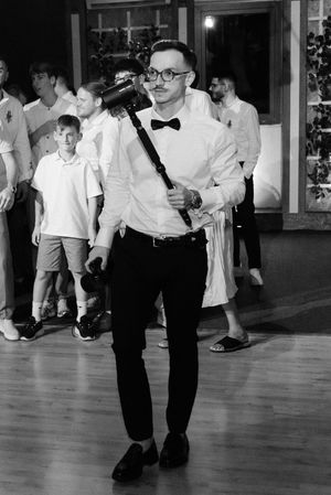 A black and white photo of a person in a bow tie and glasses dancing at an indoor event venue.