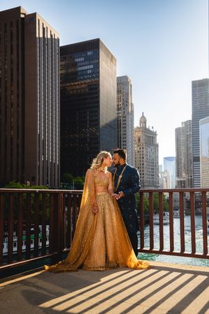 A couple in formal attire share a romantic moment on a Chicago bridge with iconic skyscrapers in the background.