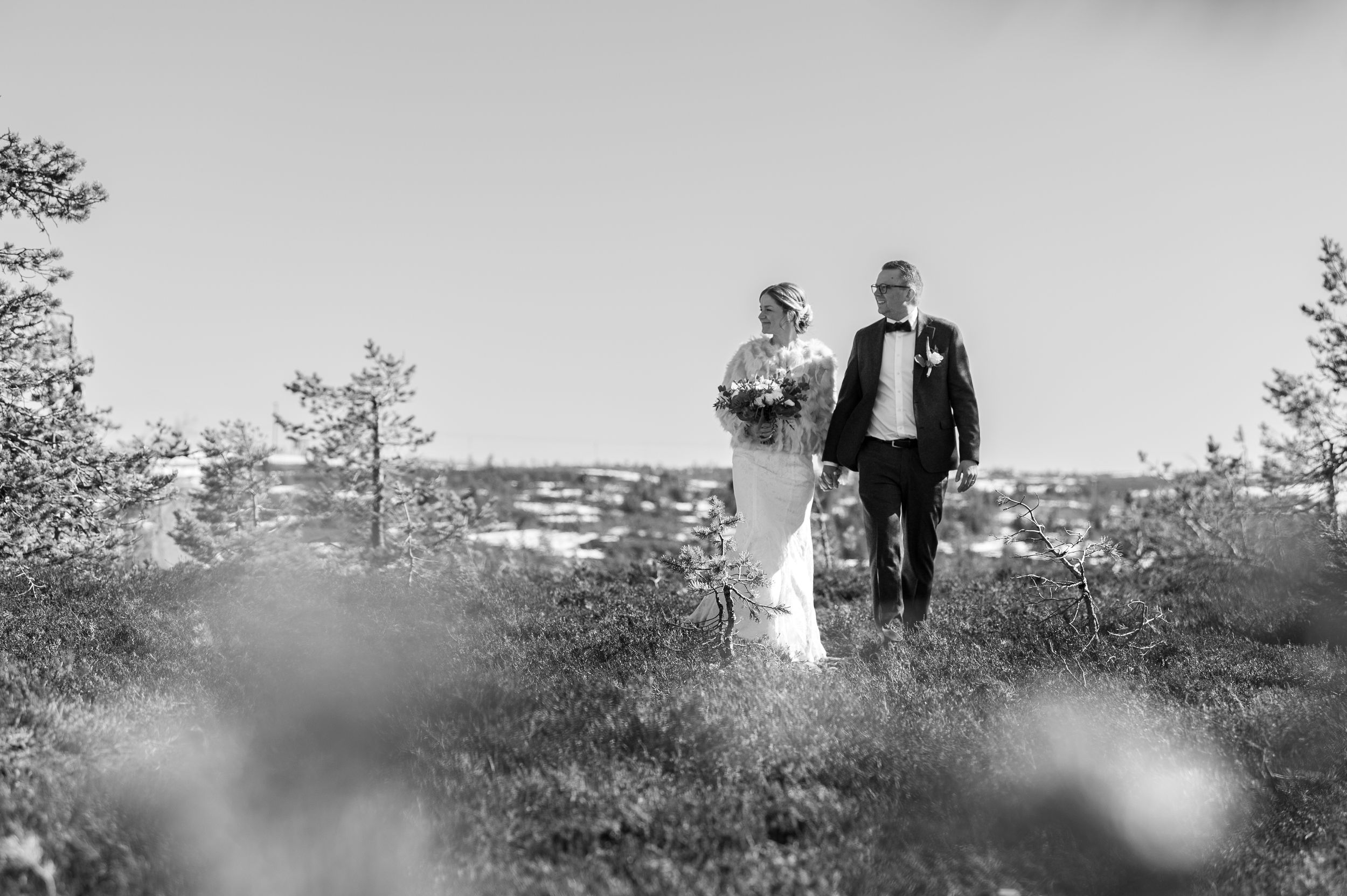 A black and white wedding photo series showing a couple walking through a scenic outdoor landscape with trees.