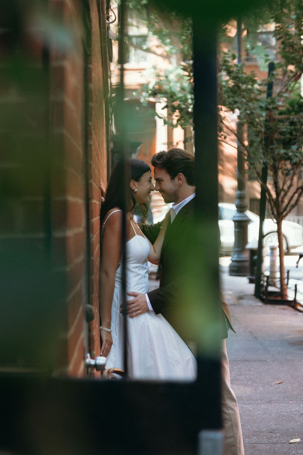 A romantic moment captured through trees on an urban sidewalk.