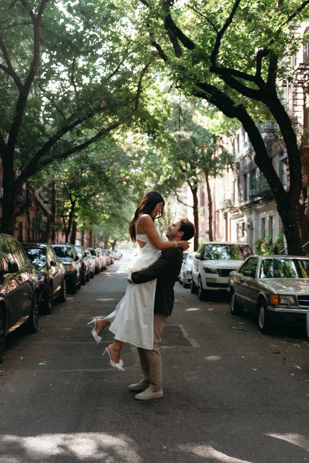 A couple performs dance lifts and spins on a tree-lined city street.