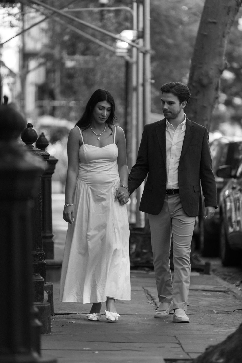 A couple takes a romantic stroll down a city sidewalk, dressed in elegant white and dark attire.