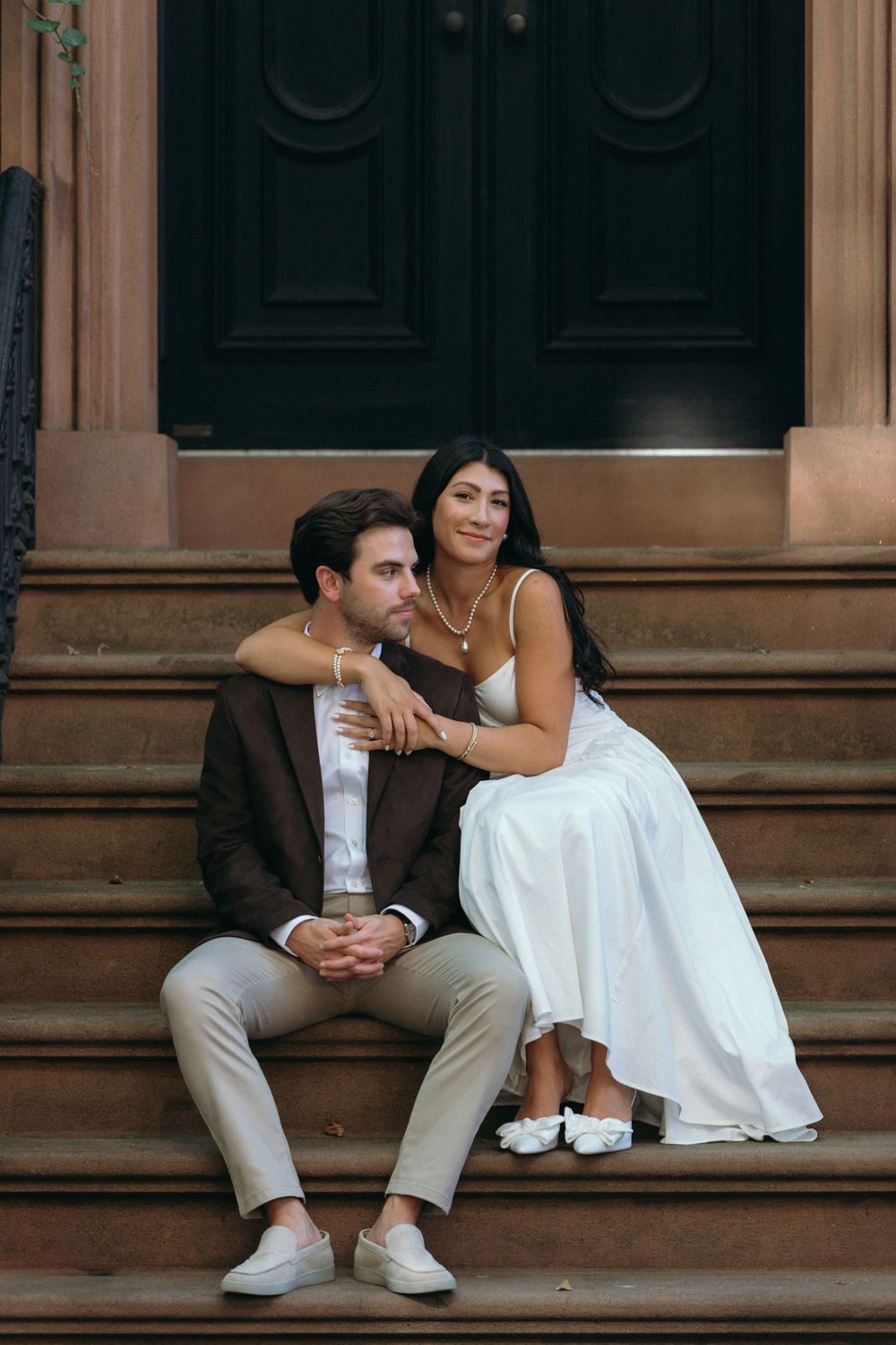 A couple sits together on brownstone steps, sharing an intimate moment in formal wear.