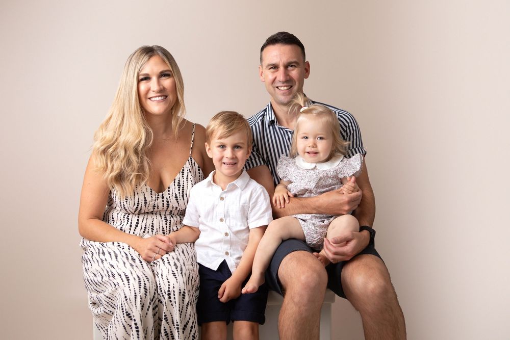 Happy family of four with two young children posing together in professional studio portrait.