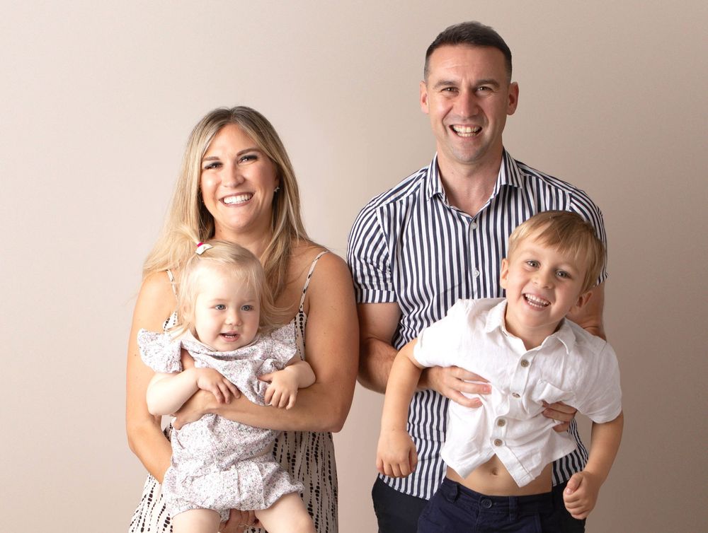Smiling family of four with baby and young boy posing for professional studio family portrait.