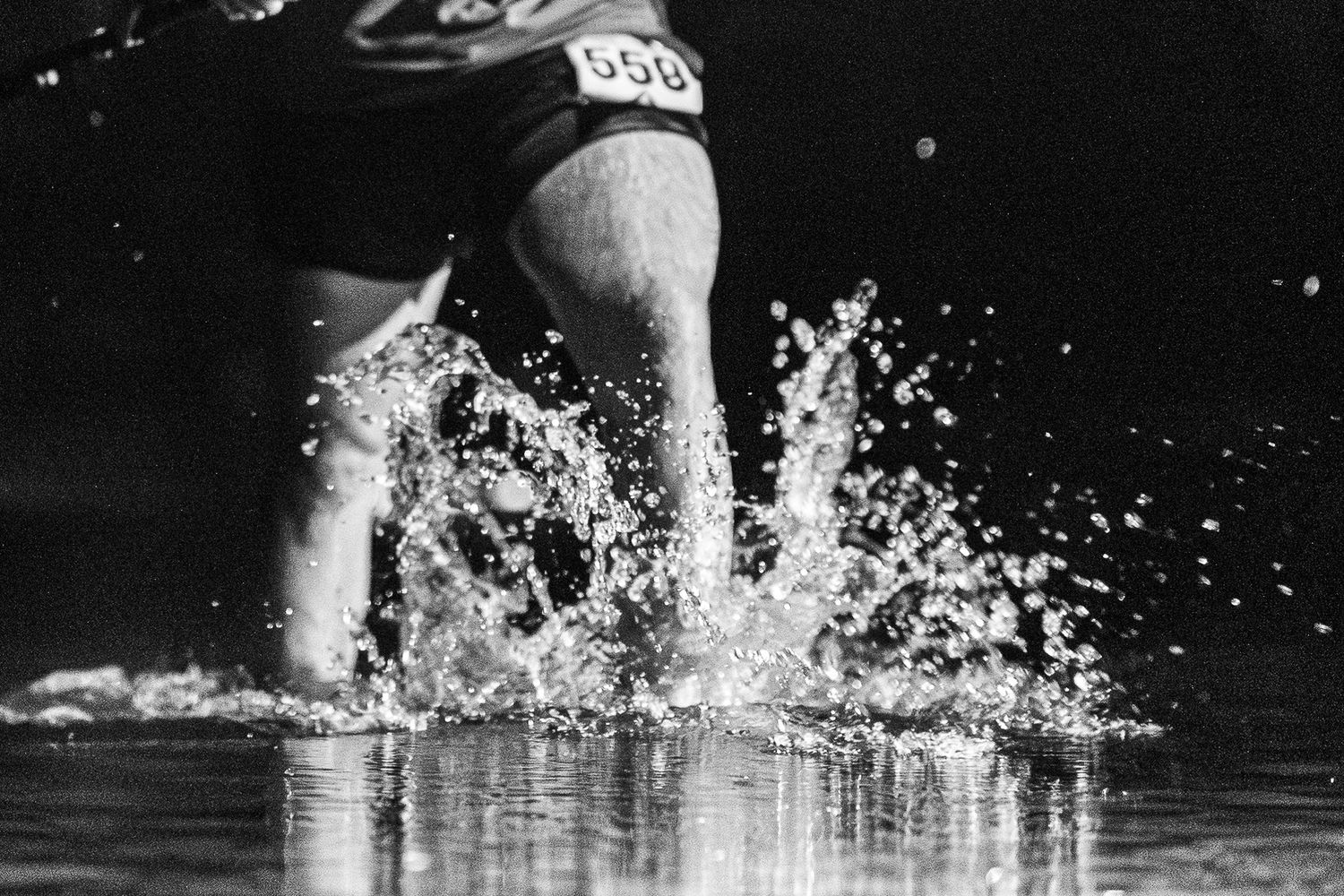 Silhouetted swimmers create dramatic splashes in dark water during competitive swimming race.