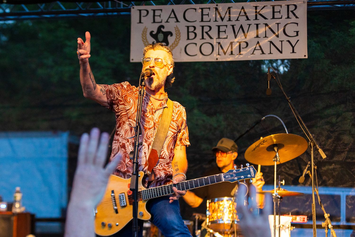 Musician performs with guitar under Peacemaker Brewing Company banner at outdoor concert.