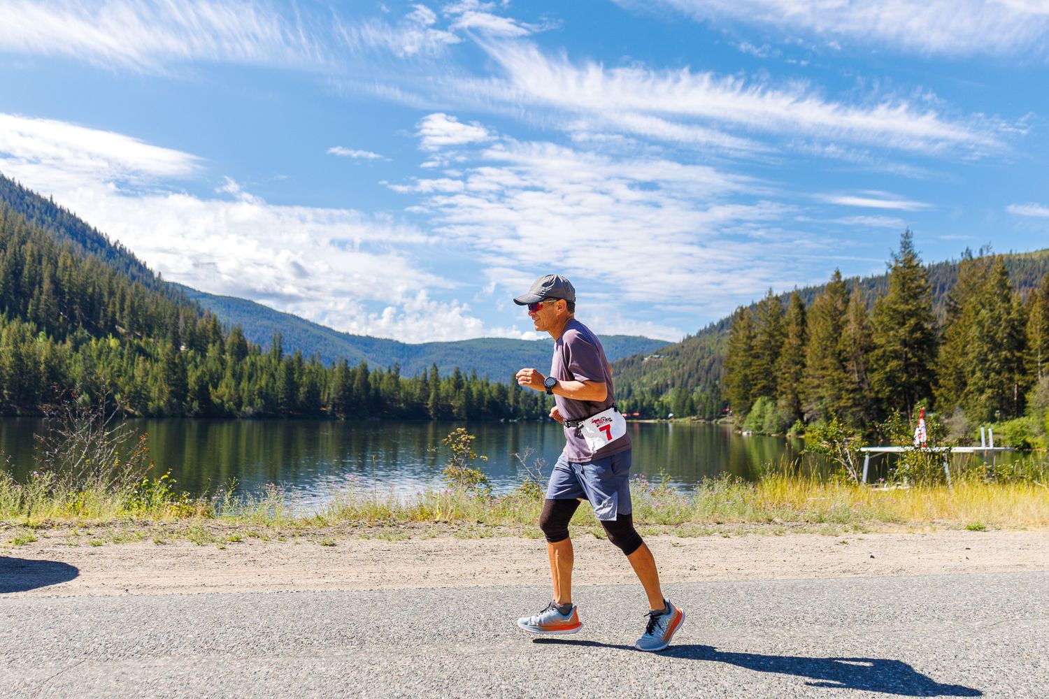 Person skips stones across a serene mountain lake surrounded by evergreen forests on a sunny summer day.