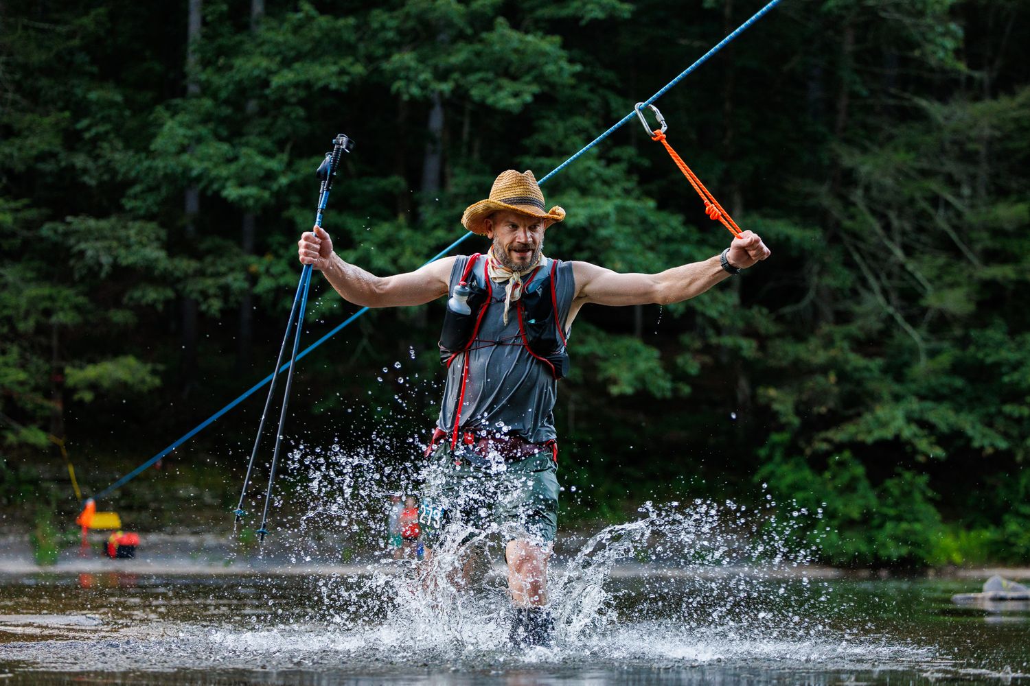 A person splashes through water while holding onto zipline cables at an outdoor adventure course.