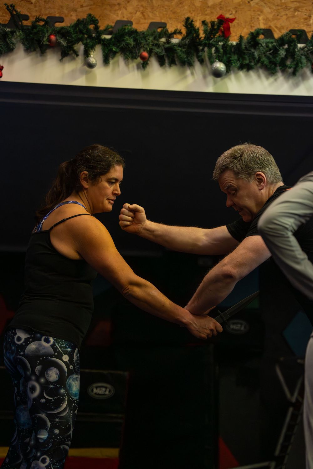 Two people demonstrating martial arts techniques with holiday decorations in background.