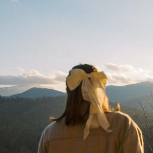 Person with a yellow bow in their hair looking at mountain landscape during sunset.