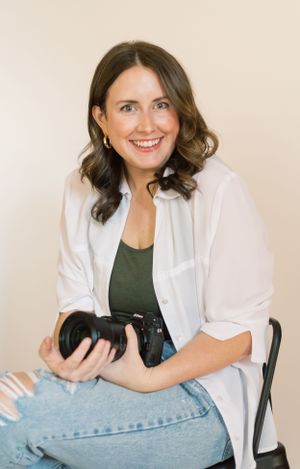 Professional photographer in white shirt holding camera while seated.