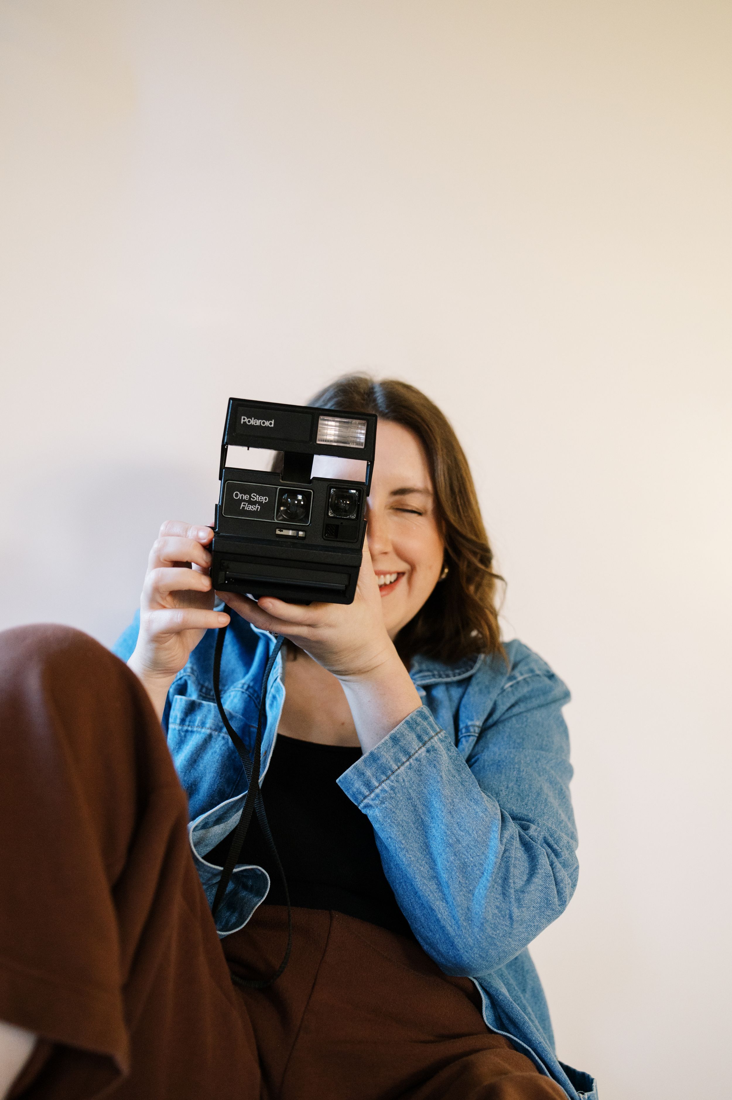 Person holding vintage Polaroid camera while smiling behind it.