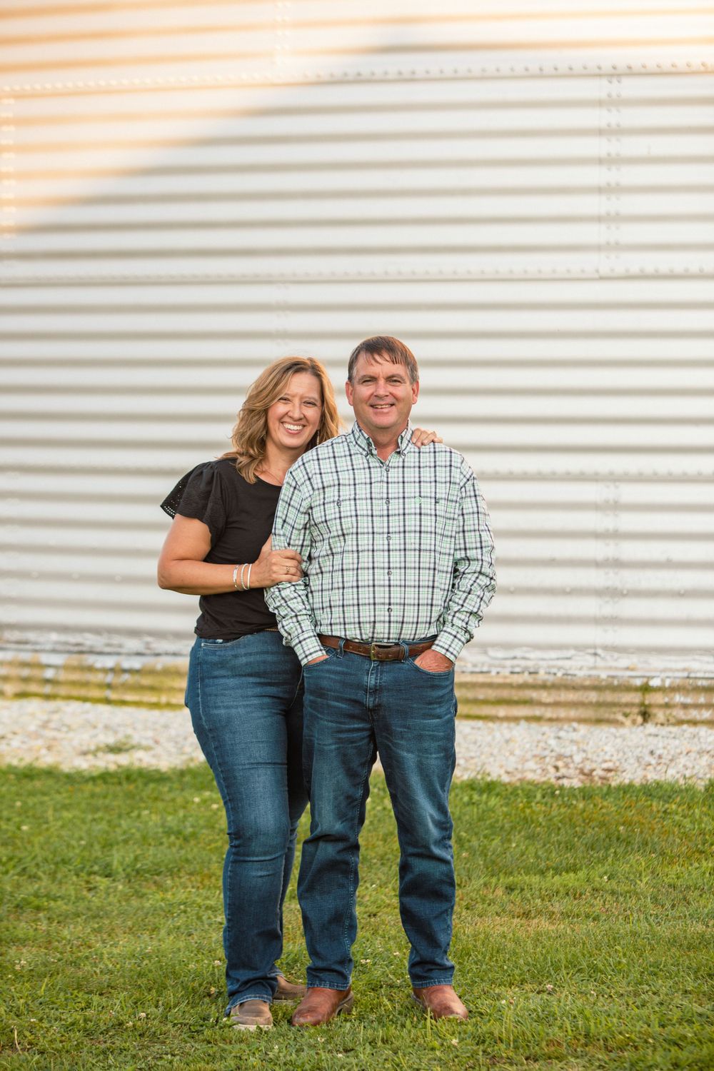 Two people in casual attire stand together in front of a metal grain silo.